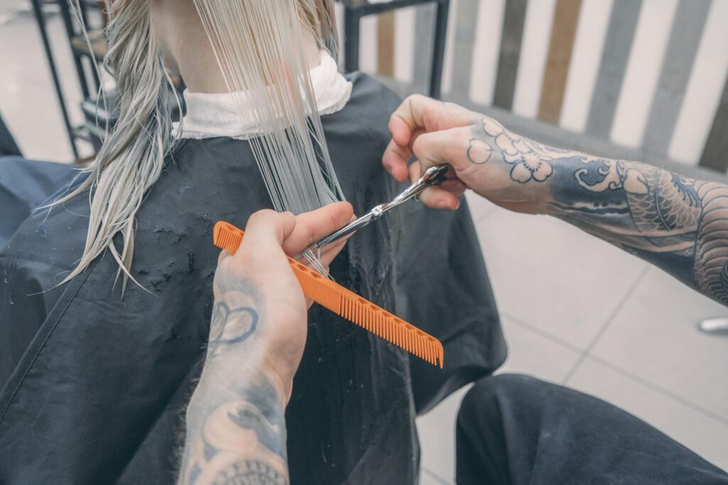 Close-up of a stylist's tattooed hands cutting wet hair in a modern beauty salon.